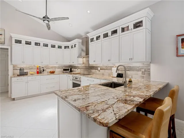 Kitchen with sink, stainless steel oven, backsplash, and wall chimney exhaust hood