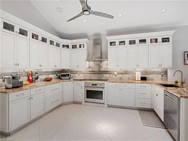 Kitchen featuring appliances with stainless steel finishes, tasteful backsplash, white cabinets, wall chimney range hood, and sink