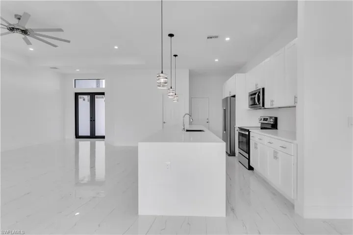 Kitchen with a kitchen island with sink, stainless steel appliances, sink, decorative light fixtures, and white cabinets