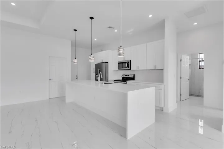Kitchen with white cabinets, hanging light fixtures, an island with sink, sink, and stainless steel appliances