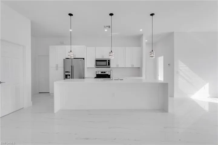 Kitchen featuring an island with sink, stainless steel appliances, sink, decorative light fixtures, and white cabinetry