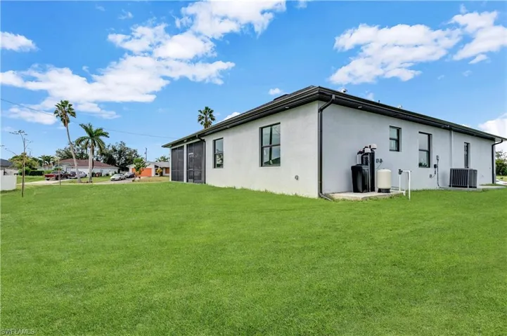 Rear view of house featuring central air condition unit and a lawn