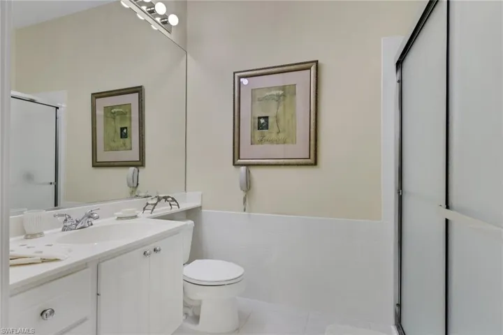 Bathroom featuring a stall shower, vanity, light tile patterned floors, tile walls, and wainscoting