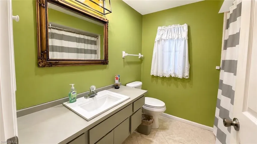 Bathroom featuring a vanity with an integrated sink, a large ornate framed mirror, a toilet, and light-toned floor tiles