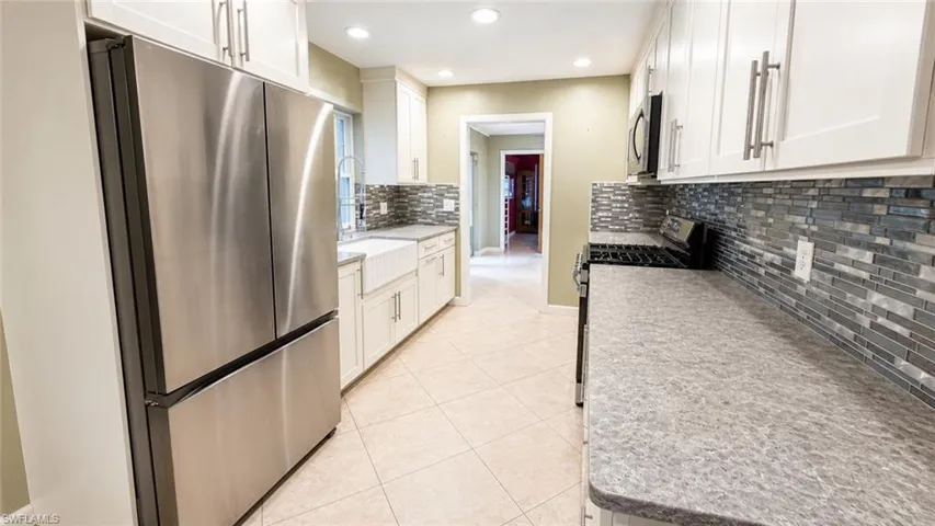Kitchen featuring stainless steel appliances, white cabinetry, a farmhouse sink, tile flooring, and a mosaic tile backsplash
