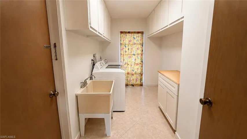 Utility room featuring a built-in wash basin, white upper cabinetry, white lower cabinetry with a wood-finish countertop, and tile flooring