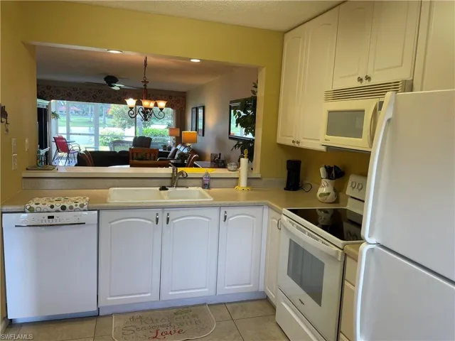Kitchen featuring white appliances, light tile patterned floors, white cabinets, decorative light fixtures, and light countertops