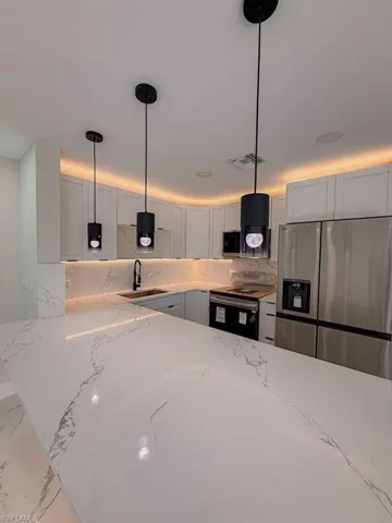 Kitchen with stainless steel appliances, light stone countertops, decorative light fixtures, and white cabinets