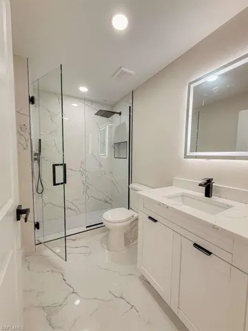 Full bathroom featuring vanity, a marble finish shower, recessed lighting, and light marble finish flooring