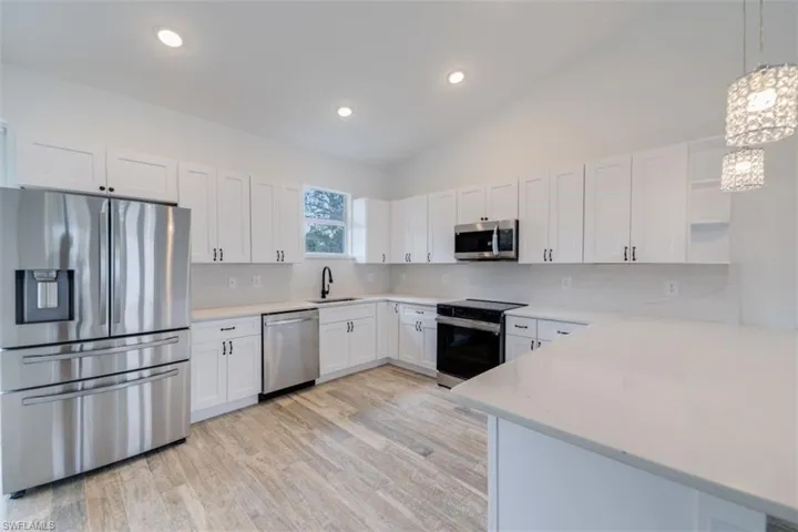 Kitchen with sink, hanging light fixtures, appliances with stainless steel finishes, tasteful backsplash, and white cabinetry