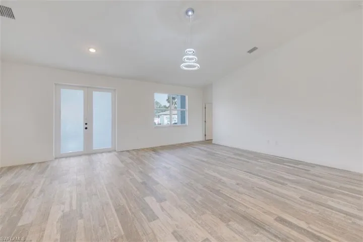 Empty room with french doors, light hardwood / wood-style flooring, and lofted ceiling