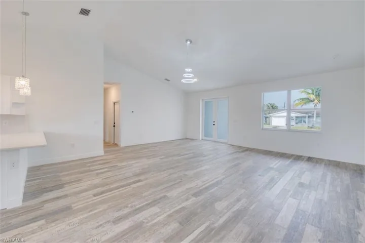 Unfurnished living room with lofted ceiling, light wood-type flooring, and an inviting chandelier