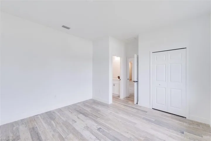 Unfurnished bedroom with connected bathroom, light hardwood / wood-style flooring, and a closet