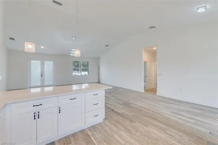 Kitchen with light wood-type flooring, vaulted ceiling, pendant lighting, a notable chandelier, and white cabinets