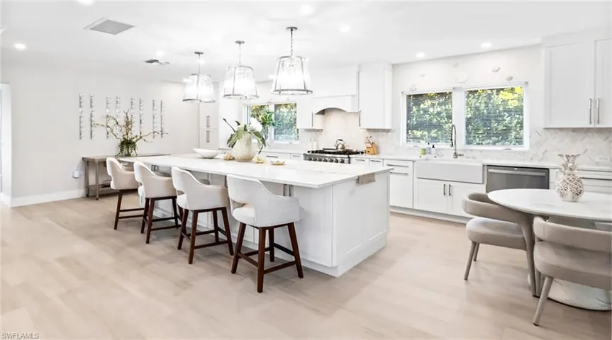 Kitchen featuring white cabinetry, a kitchen island, hanging light fixtures, a kitchen bar, and tasteful backsplash