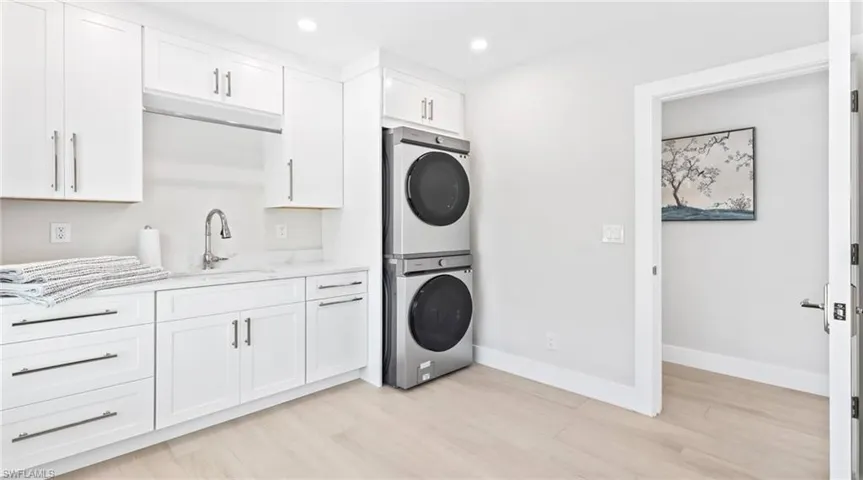 Laundry room featuring stacked washing machine and dryer, recessed lighting, light wood-type flooring, and cabinet space