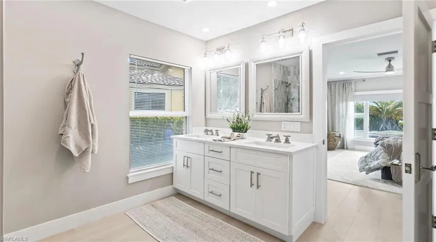 Ensuite bathroom featuring double vanity, ceiling fan, light wood-style floors, and a shower