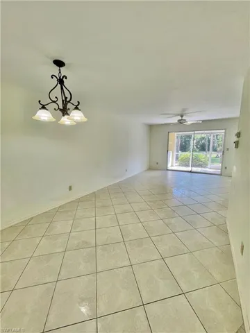 Empty room featuring ceiling fan with notable chandelier and light tile floors