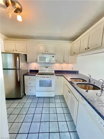 Kitchen featuring sink, white appliances, white cabinetry, and light tile floors