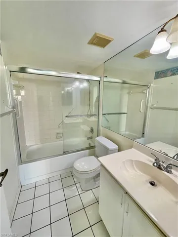 Full bathroom with tile flooring, shower / bath combination with glass door, toilet, and vanity with extensive cabinet space