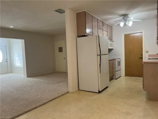Kitchen with sink, white appliances, light colored carpet, and ceiling fan