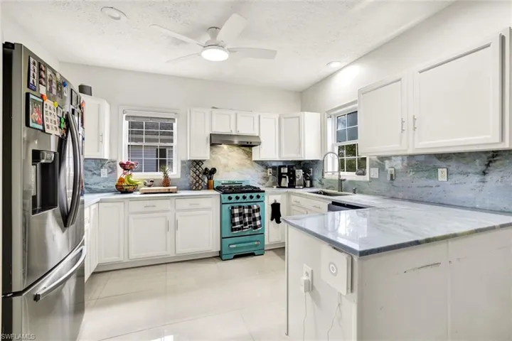 Kitchen with stainless steel fridge, range with gas stovetop, white cabinets, a peninsula, and a textured ceiling