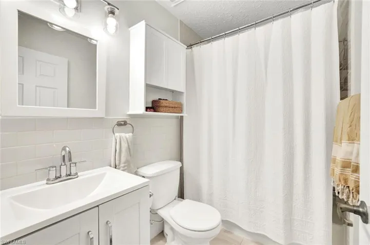 Bathroom featuring vanity, tile walls, a textured ceiling, and backsplash