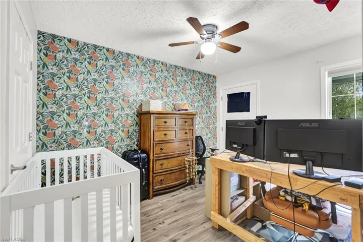 Bedroom with light wood-style floors, a textured ceiling, a nursery area, wallpapered walls, and a desk