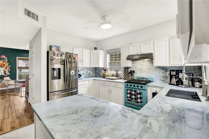 Kitchen featuring stainless steel refrigerator with ice dispenser, white cabinetry, range with gas stovetop, a ceiling fan, and light stone counters