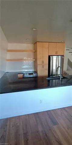 Kitchen featuring light wood finish cabinetry, stainless steel appliances, backsplash, dark wood-style flooring, and dark stone countertops