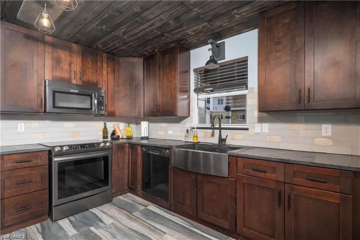 Kitchen featuring light hardwood / wood-style floors, appliances with stainless steel finishes, backsplash, dark brown cabinetry, and sink
