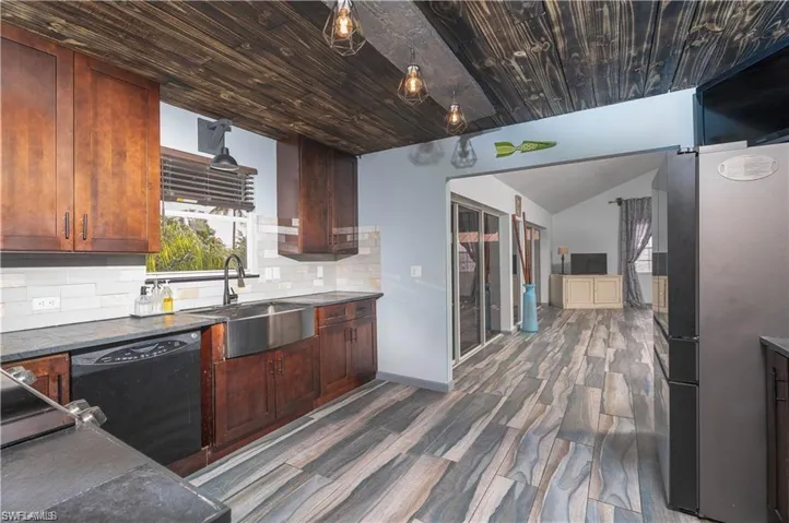 Kitchen with stainless steel fridge, dark wood-type flooring, black dishwasher, backsplash, and sink