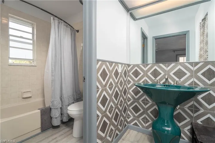 Bathroom with shower / bath combo with shower curtain, toilet, hardwood / wood-style flooring, and tile walls