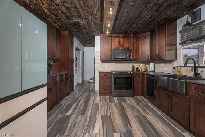 Kitchen with dark brown cabinets, stainless steel appliances, dark hardwood / wood-style flooring, backsplash, and sink