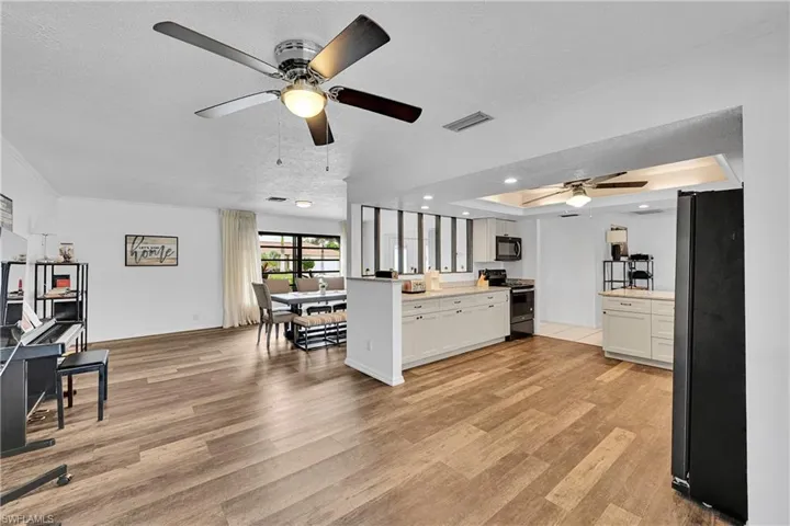 Kitchen featuring white cabinets, open floor plan, black appliances, light wood-type flooring, and a tray ceiling