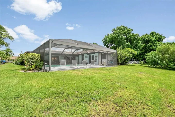 Rear view of house featuring an outdoor pool, a sunroom, a lawn, and glass enclosure