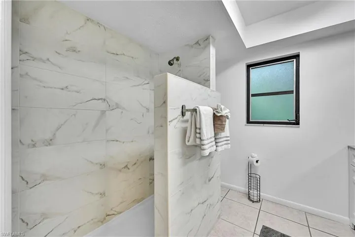 Bathroom featuring a marble finish shower, light tile patterned floors, and a textured ceiling
