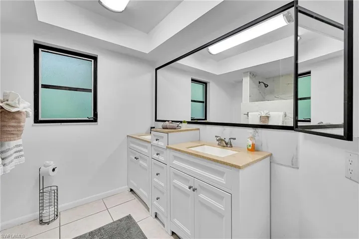 Bathroom with double vanity, light tile patterned floors, a raised ceiling, and a marble finish shower