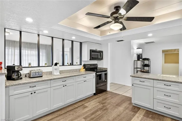 Kitchen with white cabinetry, stainless steel electric stove, light stone counters, recessed lighting, and black microwave