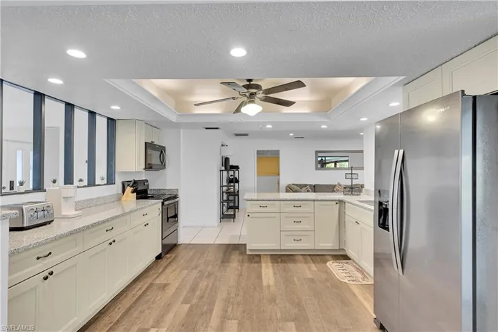 Kitchen featuring appliances with stainless steel finishes, a peninsula, a raised ceiling, light stone countertops, and light wood-style floors