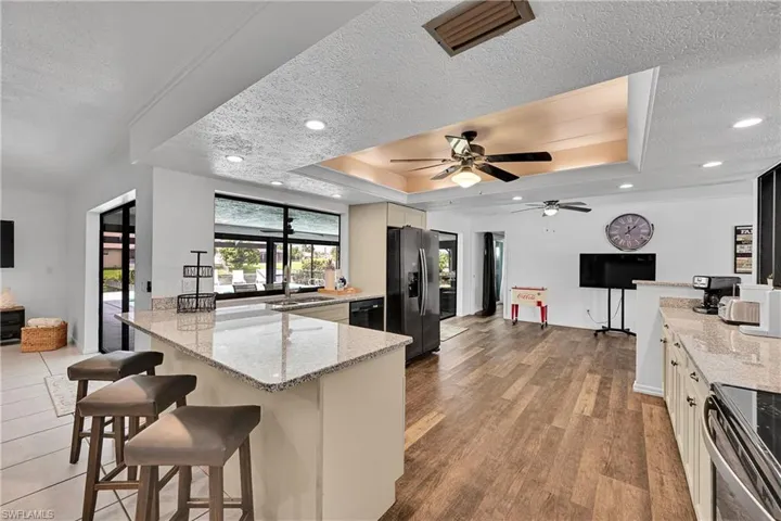 Kitchen featuring a tray ceiling, light stone countertops, a peninsula, a textured ceiling, and appliances with stainless steel finishes