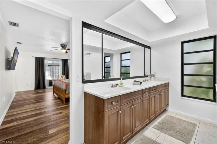 Full bathroom with ensuite bathroom, double vanity, a tray ceiling, and ceiling fan