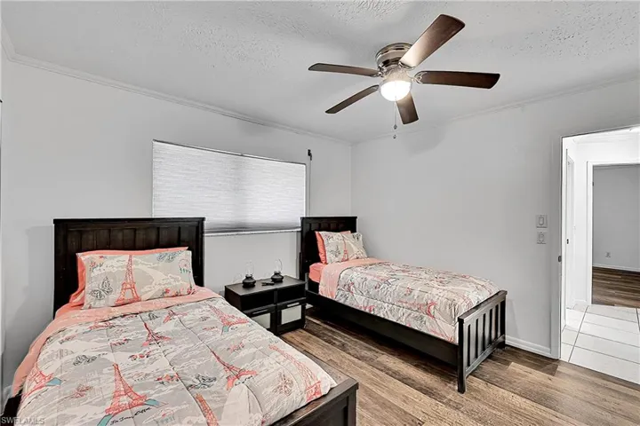 Bedroom featuring wood finished floors, a textured ceiling, ornamental molding, and a ceiling fan