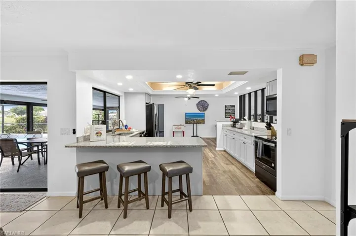 Kitchen with a kitchen breakfast bar, a tray ceiling, light stone countertops, a peninsula, and crown molding