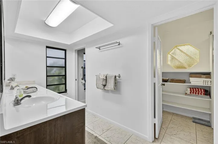 Bathroom featuring a closet, double vanity, light tile patterned floors, and a tray ceiling
