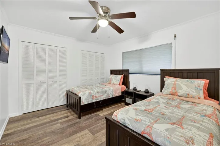 Bedroom featuring multiple closets, ornamental molding, wood finished floors, and ceiling fan