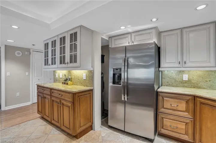 Kitchen featuring backsplash, light stone countertops, stainless steel fridge with ice dispenser, and light tile flooring