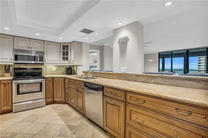 Kitchen with a raised ceiling, light stone countertops, stainless steel appliances, and sink