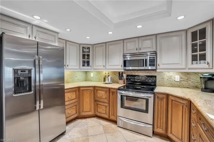 Kitchen with light stone countertops, stainless steel appliances, a raised ceiling, backsplash, and light tile floors