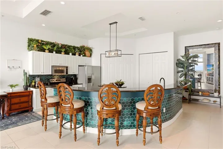 Kitchen with a breakfast bar area, stainless steel appliances, white cabinetry, a large island with sink, and dark stone countertops